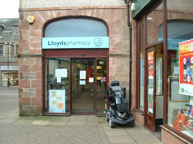 Eine Apotheke mit einem vor ihr geparkten Fahrzeug und einem Geb√§ude in der linken Ecke.