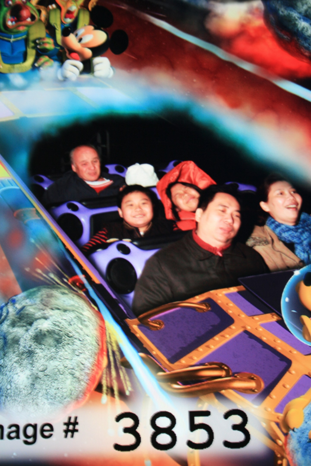 Gruppe von Menschen auf einer Achterbahn mit Mickey-Maus-Figuren im Hintergrund und Text unten.