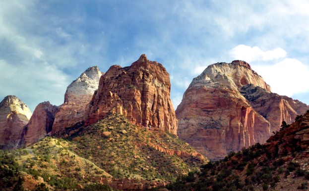 Ein malerischer Blick auf den Zion-Nationalpark in Utah mit majestätischen Bergen, grünen Bäumen, steiniger Landschaft und weißen Wolken am Himmel.