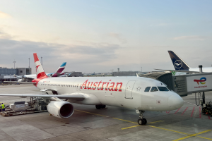 Ein Austrian-Airlines-Airbus-A330-300 auf dem Rollfeld am Frankfurter Flughafen, umgeben von Menschen, Fahrzeugen und anderen Gegenständen, mit Gebäuden, Polen und einem klaren blauen Himmel im Hintergrund.
