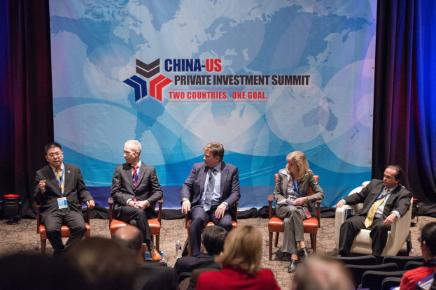 Eine Gruppe von Menschen, die auf Stühlen sitzen und auf einen Bildschirm schauen, auf dem Text und eine Karte angezeigt werden, mit Vorhängen im Hintergrund, was auf einen China-US-Privatinvestmentgipfel hindeutet.