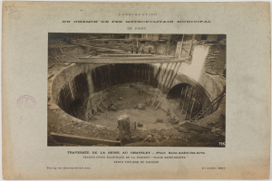 Ein altes Schwarz-Weiß-Foto eines Tunnels im Bau, mit einem Stempel auf der linken Seite und Text unten.