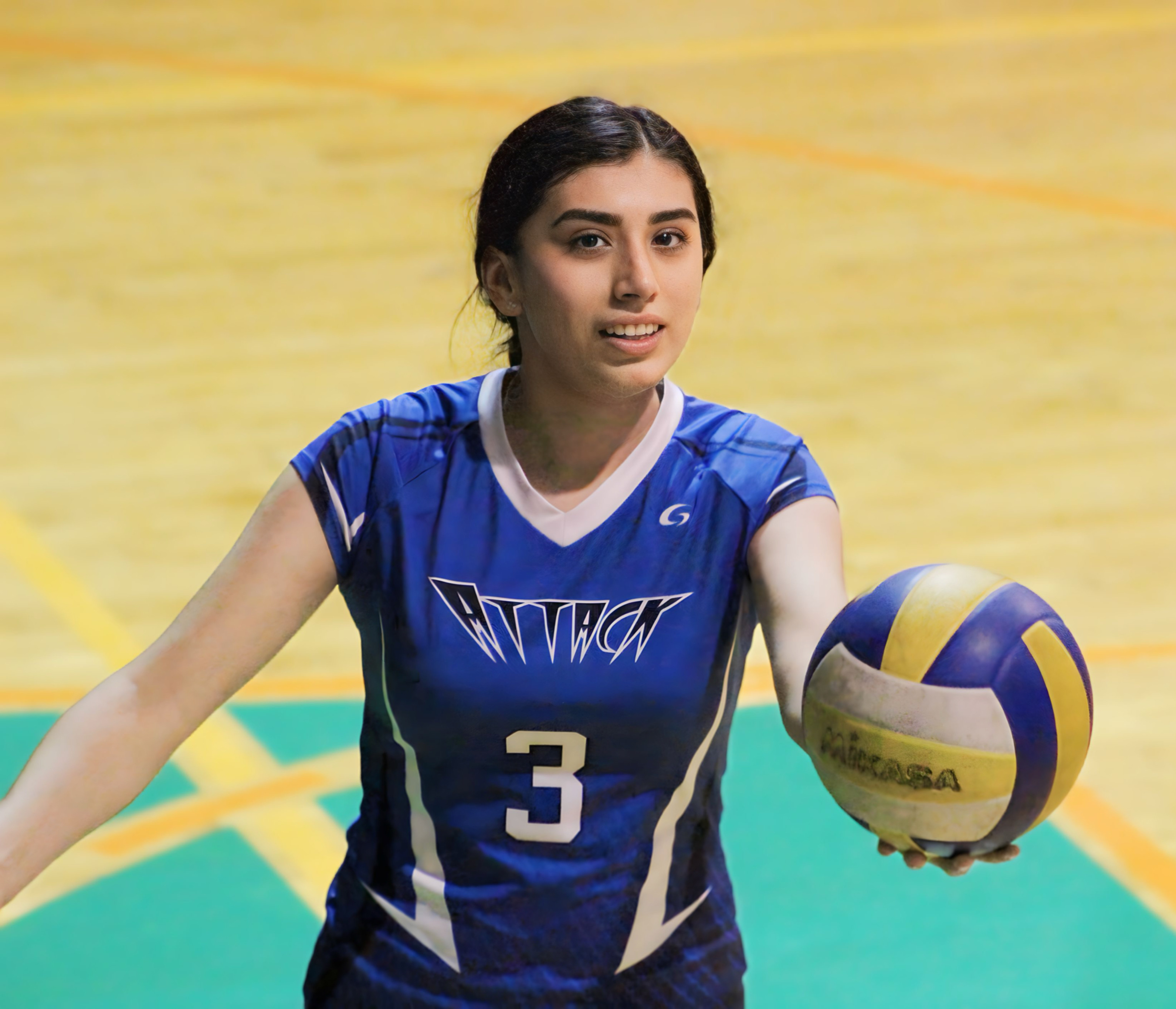 Eine Frau in einem blauen T-Shirt und Pferdeschwanz steht auf einem Volleyballfeld, hält einen Volleyball und hat einen entschlossenen Gesichtsausdruck.
