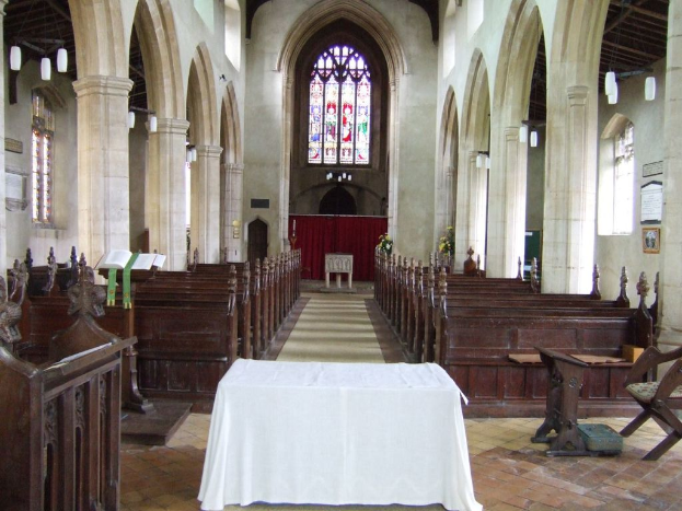 Ein Raum mit Tischen, einem Podium, einem Buchständer, Stühlen, Bänken, Säulen, Tafeln, einem Vorhang, Fenstern, Stoff, Pflanzen und diversen Gegenständen.