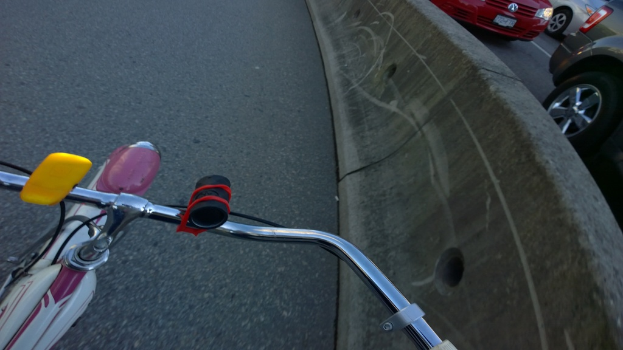 Ein Fahrradlenker befindet sich unten im Bild, mit Fahrzeugen, die auf der rechten Seite fahren, und einer Mittellinie in der Mitte.