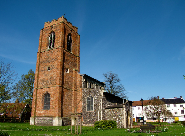 Eine grasbewachsene Fläche mit einem Mast, Gebäuden und Bäumen im Hintergrund.