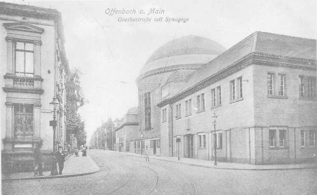 Schwarzes und weißes Foto einer Stadtstraße mit der Beschriftung "Offenbach a.M., Goethestraße mit Synagoge", das Gebäude, Straßenlaternen, Lichter, Bäume und Fußgänger zeigt.