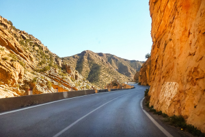 Winding road through a rocky gorge with hills on either side and a clear blue sky.